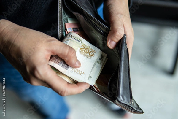 Obraz Person holding a 200 PLN banknote near an open leather wallet. Image symbolizes cash handling, personal finances