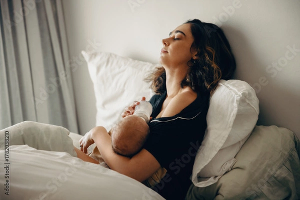 Obraz Tired mother bottle-feeding baby while resting in bed
