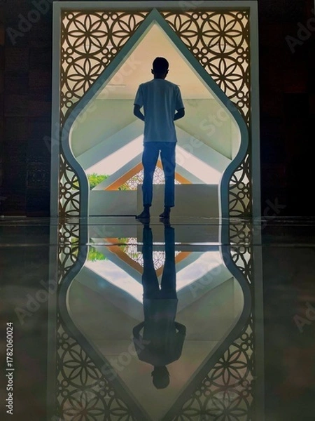 Obraz Peaceful scene of a man standing in a mosque doorway with geometric Islamic patterns and reflection on polished floor. Represents devotion, serenity, and harmony in spiritual architecture.