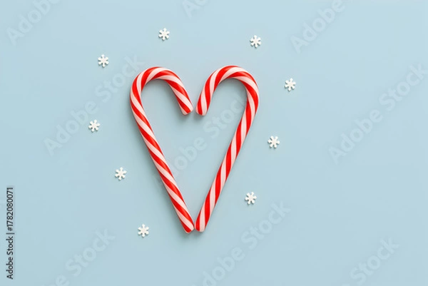 Fototapeta Two candy canes are arranged in a heart shape with snowflakes on a light blue background for christmas, christmas