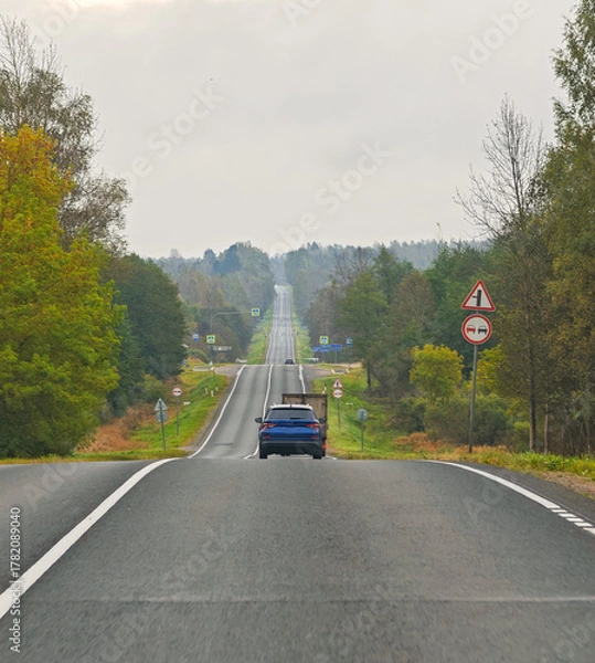 Fototapeta Country road view from car with truck and car autumn landscape horizontal frame