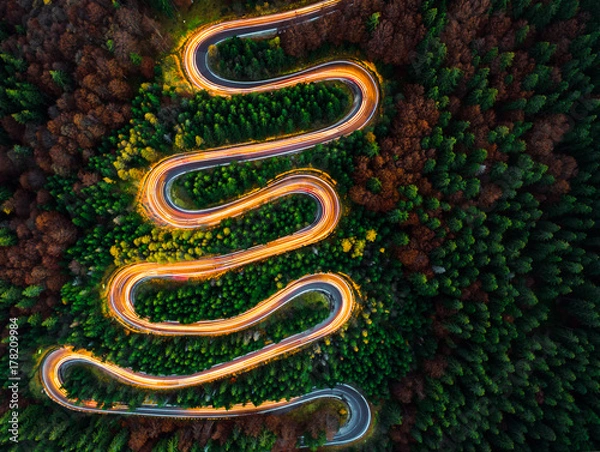 Obraz Aerial view of light trails on a winding road through the forest in fall