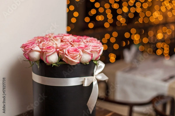 Obraz A bouquet of roses in a hat box in a dark room against the background of bokeh lights