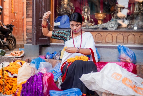 Obraz Newari Girl in traditional attire Crafting Globe Amaranth Garlands(makhmali flower) for Bhai Tika in tihar
