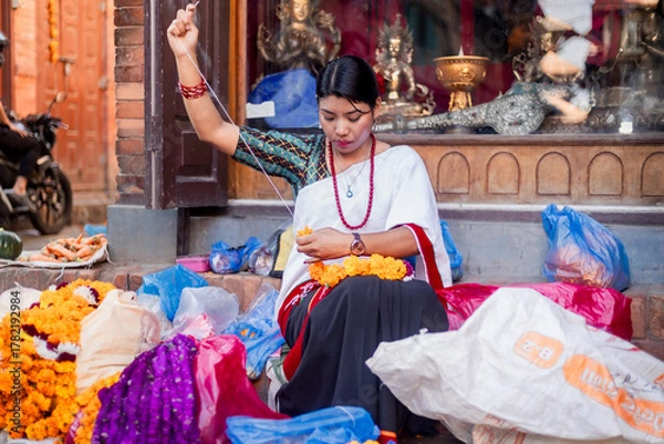 Obraz Newari Girl in traditional attire Crafting Globe Amaranth Garlands(makhmali flower) for Bhai Tika in tihar
