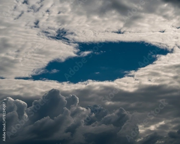 Fototapeta Dramatic sky with a vibrant blue opening amidst billowing clouds, suggesting hope and transition.