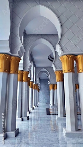 Obraz Interior view of a mosque corridor with white marble floors, golden pillars, and ornate arches. A stunning display of Islamic architecture and peaceful spiritual harmony.