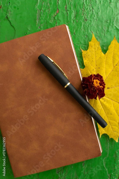 Fototapeta Pen, brown-covered notebook, marigold and yellow maple leaf