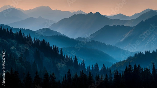 Fototapeta Layered mountain ranges with evergreen trees and a hazy blue atmosphere at dusk or dawn