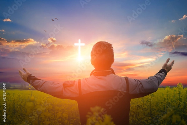 Fototapeta Christian man worshiping the christian cross in the field at sunset