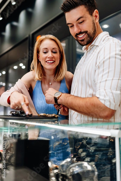 Fototapeta Elegant couple enjoying a moment in a jewelry store, trying on luxury watches while smiling and embracing, making a thoughtful purchase decision for a special occasion