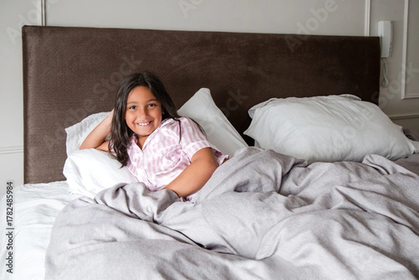 Fototapeta A young girl is laying on a bed with a blanket and a pillow