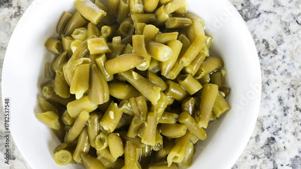 Fototapeta Fresh canned green beans in a white bowl on a marble countertop with a healthy appearance