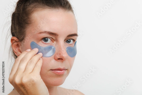 Fototapeta Close up portrait of a young european girl or woman a blue mask and patches for the skin around the eyes. Copy space