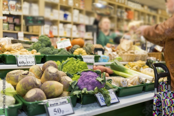 Obraz Close up of delicious and colourful vegetables with the market stall and market trader blurred in the background serving a client in England, UK