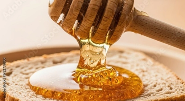 Fototapeta Honey dripping from a wooden dipper onto a slice of bread creating a golden sweet breakfast treat