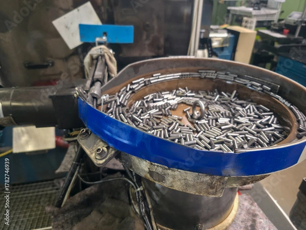 Fototapeta Industrial machine sorting metal rods in vibration feeder bowl at a factory during daytime