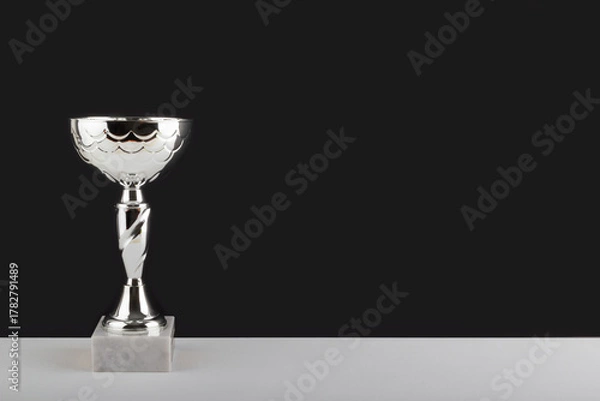 Obraz Silver winner cup on white table against black wall background.