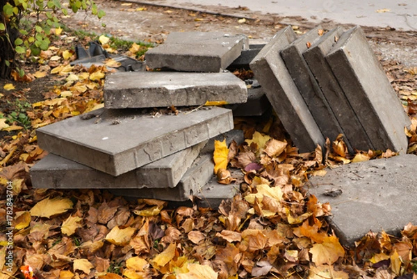 Fototapeta Stack of concrete slabs surrounded by fallen autumn leaves. Concept of construction, decay, and urban renewal in a seasonal outdoor environment