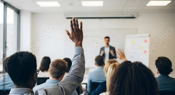 Fototapeta Close-up of a person's hand raised in the classroom, seeking attention from the speaker in front of a projector screen.