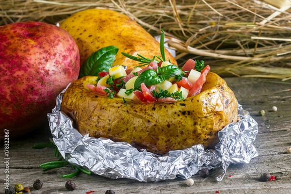 Fototapeta baked potato in foil with ham and cheese on a wooden background