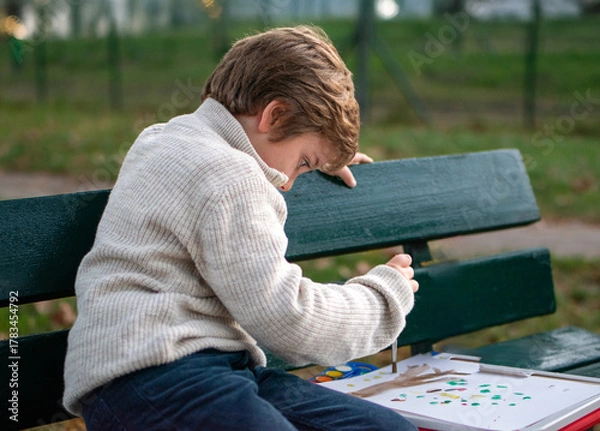 Obraz Portrait of a 7-year-old boy drawing in the park on an autumn day