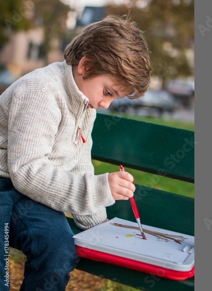 Obraz Portrait of a 7-year-old boy drawing in the park on an autumn day