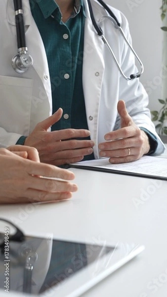 Fototapeta Doctor man wearing medical coat over green shirt, and stethoscope is gesturing with hands while explaining diagnosis to patient during medical consultation in clinic office. Medicine and health care