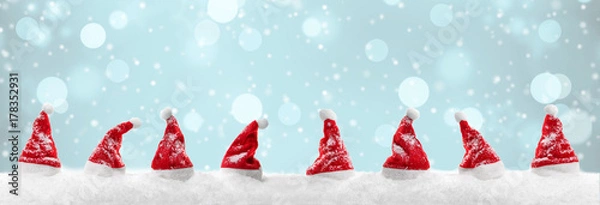 Fototapeta Czerwone czapki Mikołaja w śniegu z zimowym bokeh w tle