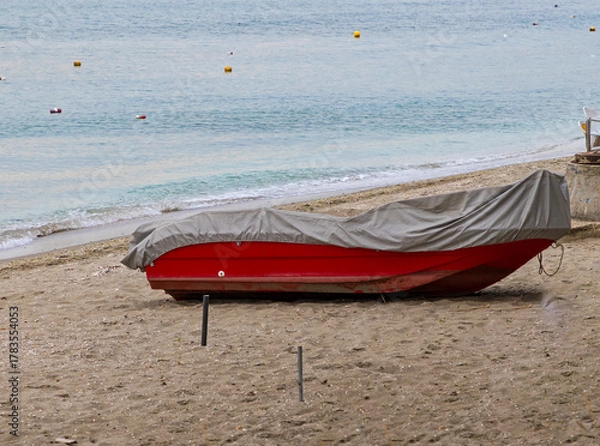 Fototapeta Skiff boat covered with plastic parked on beach send during winter