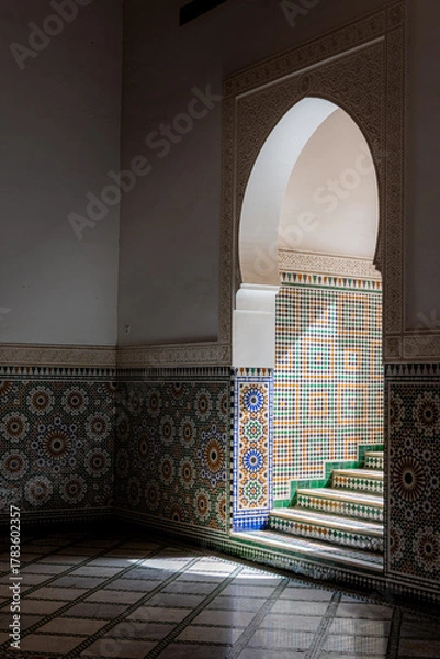 Fototapeta Hard shadows fall across an arched doorway and stairs, highlighting the geometric lines and architectural details inside the Mausoleum of Moulay Ismail in Meknes, Morocco.

