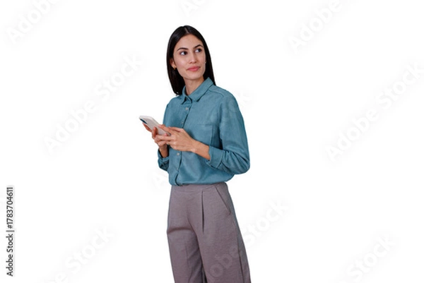Fototapeta Young businesswoman holding a phone, texting or scrolling, looking aside with a pensive expression, considering data or messages