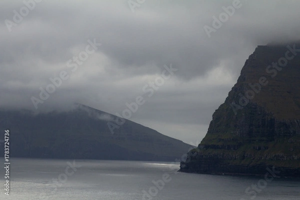Fototapeta Misty mountain rising above the sea in the Faroe Islands, capturing the wild spirit of Nordic travel and hiking adventures.