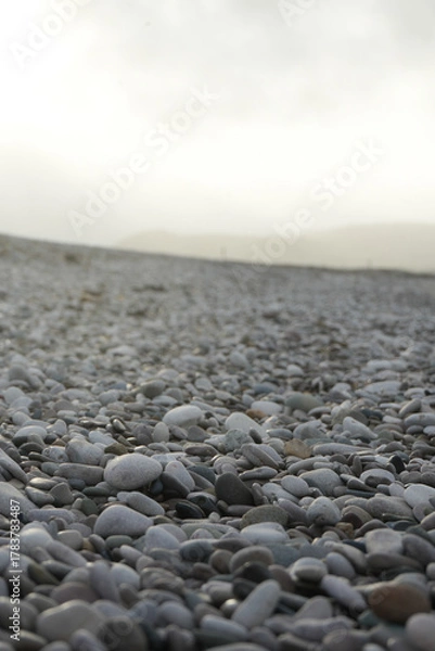 Obraz Close-up Of Smooth Grey And White Pebbles Stretching Across A Tranquil Beach Under A Hazy Sky In Towyn, North Wales, Uk.