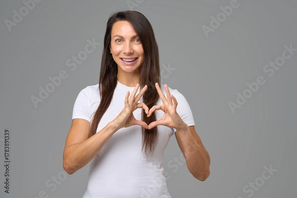 Fototapeta Smiling woman making a heart shape with fingers expressing happiness and love