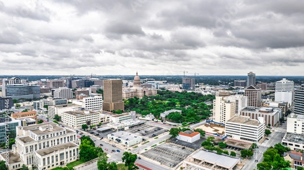 Obraz Panoramic aerial view of Austin, Texas skyline under dramatic cloudy skies. The Texas State Capitol building is prominent amidst a dense urban landscape with skyscrapers and roadways. A moody