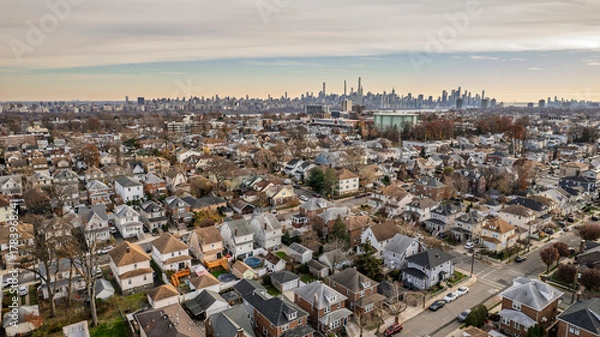Obraz Panoramic aerial view of a residential neighborhood bathed in golden hour light. Houses line streets beneath a vibrant blue sky with wispy clouds. Urban landscape, suburban serenity, peaceful
