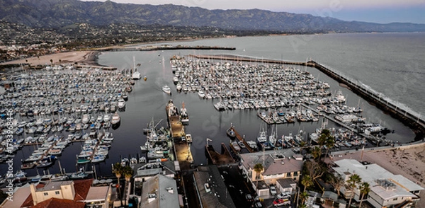 Fototapeta Aerial view of a bustling harbor filled with boats at dusk. Rolling hills in the background under a dusky sky. Reflective water adds to the serene atmosphere.