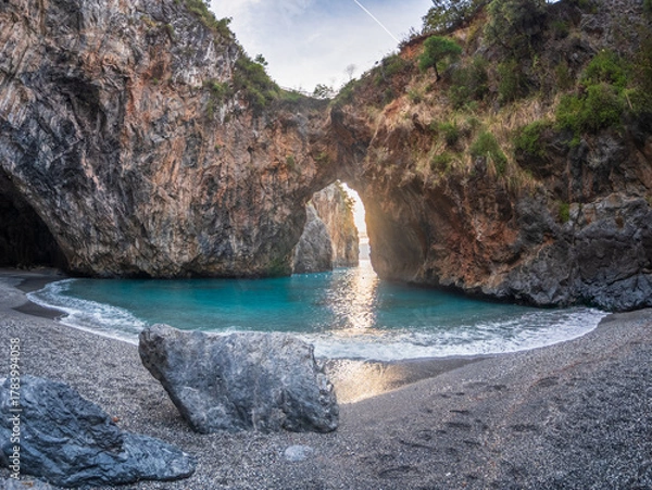 Fototapeta Arcomagno beach in Calabria Italy showing turquoise sea meeting rugged cliffs and hidden caves in backlight symbolizing untouched natural beauty