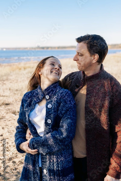 Fototapeta Loving couple walks on beach along sea on sunny autumn day. Weekend and lifestyle concept. Vertical photo. High quality photo