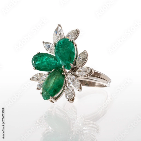 Fototapeta platinum ring with two pear-cut emeralds and one marquise-cut emerald surrounded by nine diamond navettes, isolated on white background