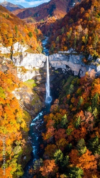Obraz Cascading waterfall surrounded by autumn foliage and rocky cliffs from an aerial perspective