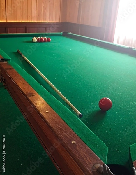 Fototapeta A close-up of a pool table showcasing green felt, wooden trim, a cue stick, and a single red ball with other balls lined up
