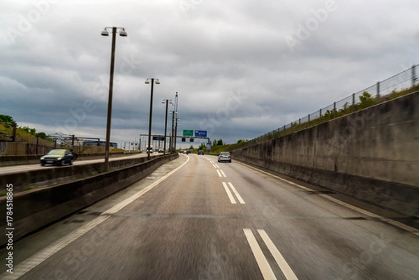Fototapeta Highway leading to the Oresund Fixed Link. Cars driving on the multi lane road under a cloudy sky, representing travel and infrastructure.