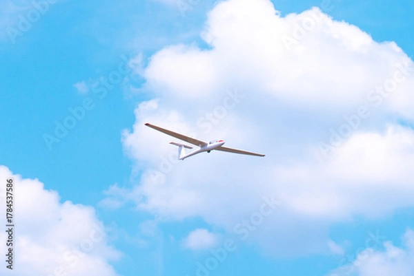 Fototapeta Small glider flying against the blue sky and clouds