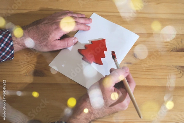 Fototapeta Hands painting red christmas tree shape on paper