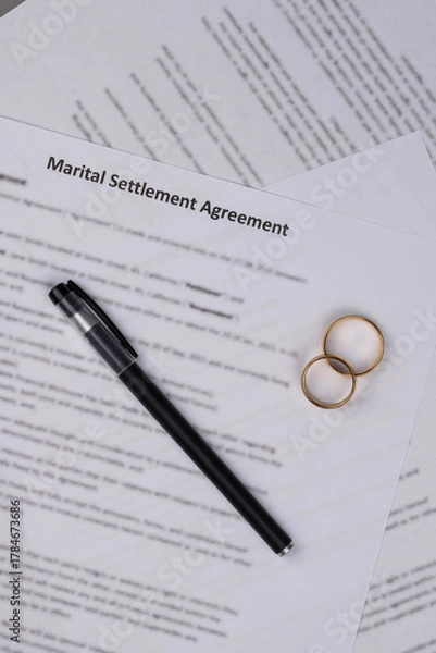 Fototapeta Marital Settlement Agreement paper document with wedding rings on table, ready for signature, symbolizing divorce, prenuptial contract, breakup, and separation.