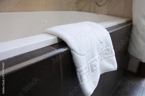 Fototapeta Foot towel. A white towel is hanging on the side of the tub. The concept of personal hygiene.