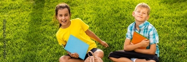 Obraz Happy child sitting on the field holding tablet. Boy sitting on the grass on sunny day. Home schooling or playing a tablet