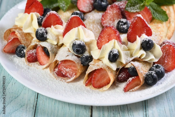 Fototapeta French crepes filled with whipped cream, strawberries, and blueberries, dusted with powdered sugar.